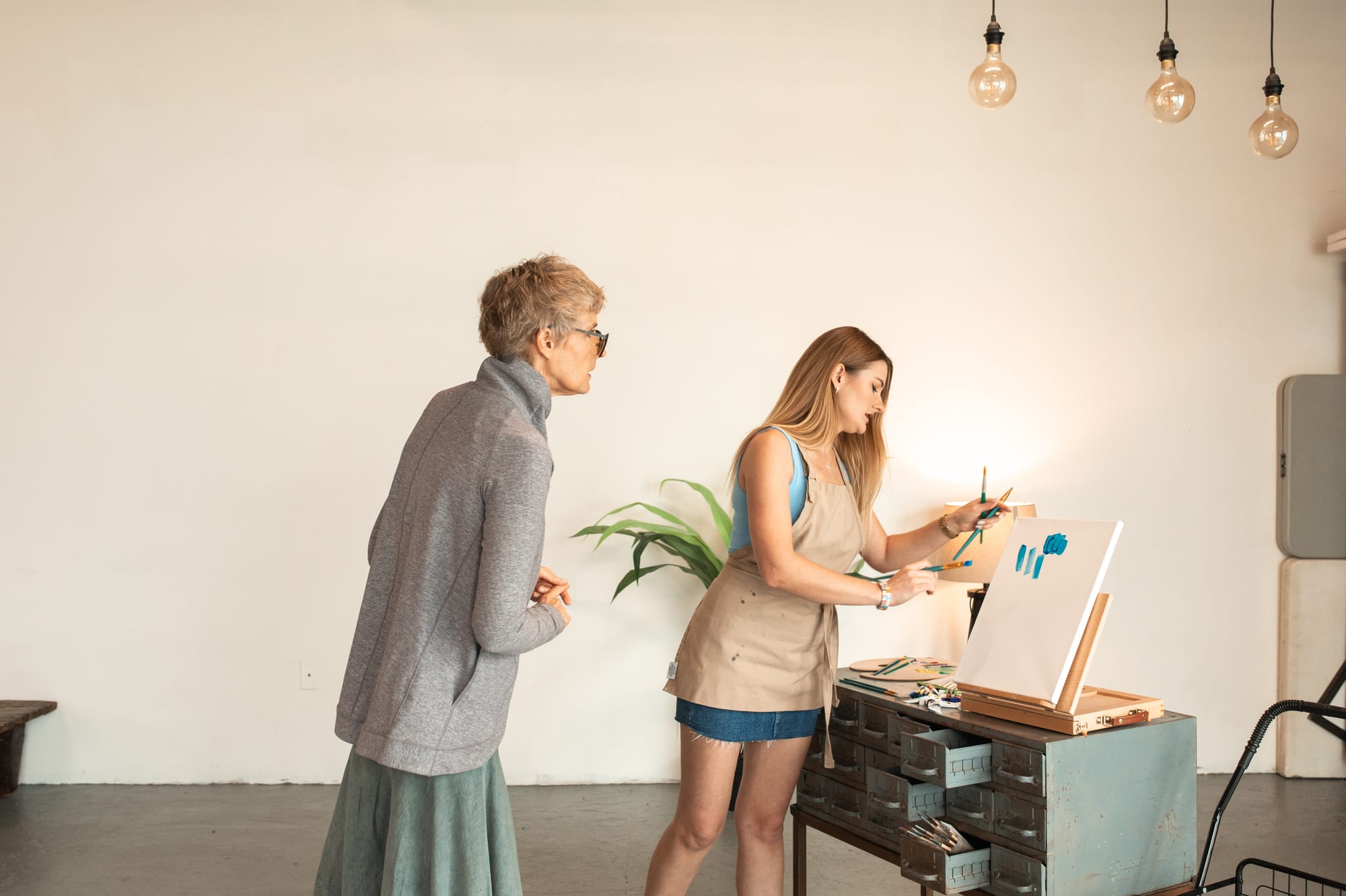Free Woman in Blue Tank Top Wearing Brown Apron Painting on White Canvas Stock Photo