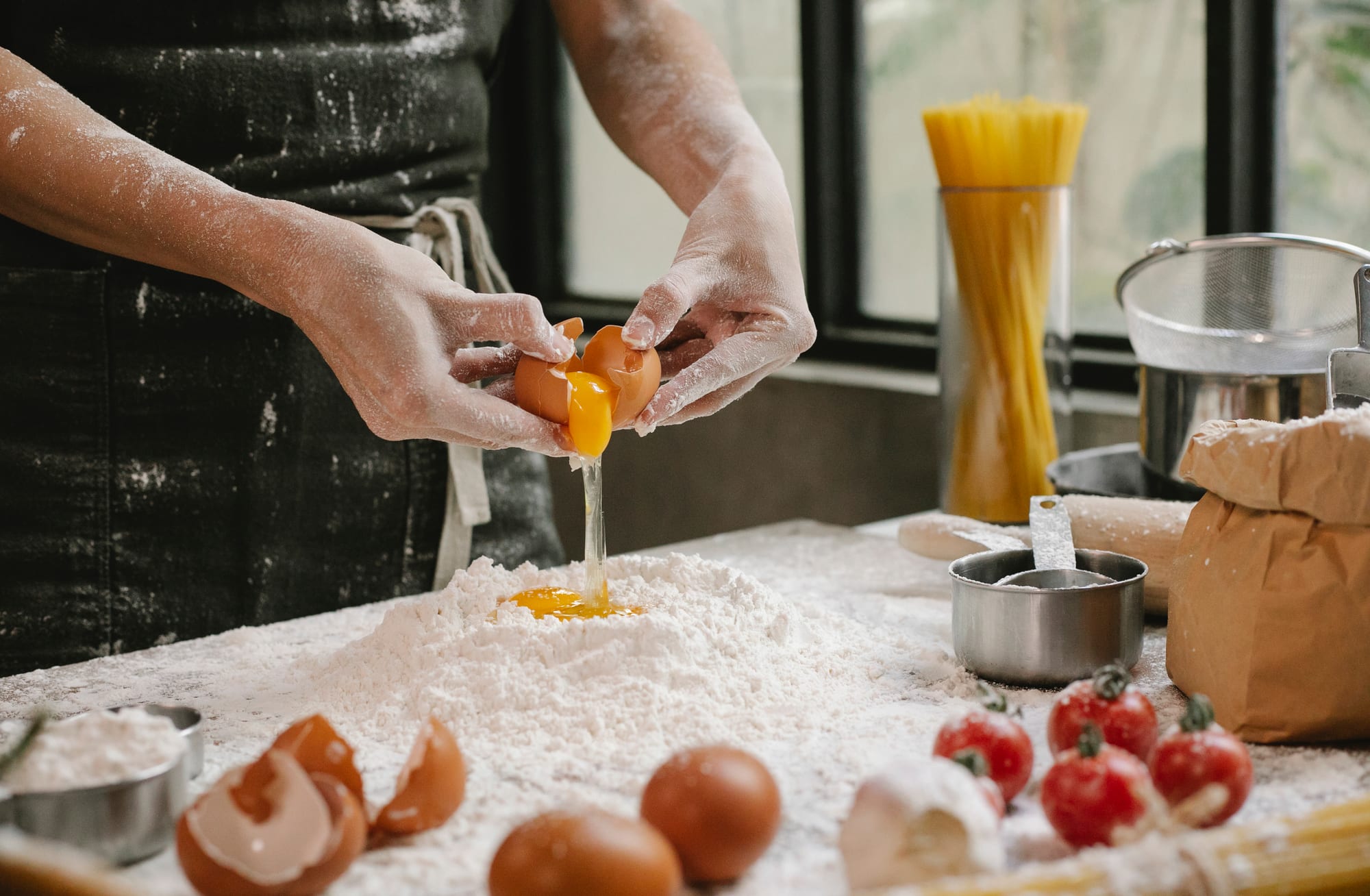 Free Crop anonymous person adding egg in flour while cooking pastry for recipe with cherry tomatoes and spaghetti Stock Photo